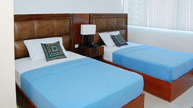 Deux lits simples avec des têtes de lit en bois, une literie bleue et des coussins décoratifs.