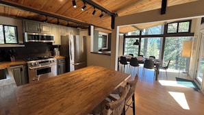 Una cocina moderna con vigas de madera en el techo, electrodomésticos de acero inoxidable y una gran mesa de comedor con sillas de mimbre.