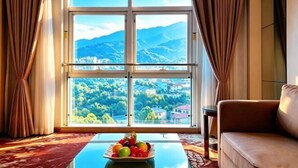 Une pièce dotée d’une grande fenêtre, d’un canapé, d’une table sur laquelle sont disposés des fruits, et offrant une vue sur les montagnes et la verdure.