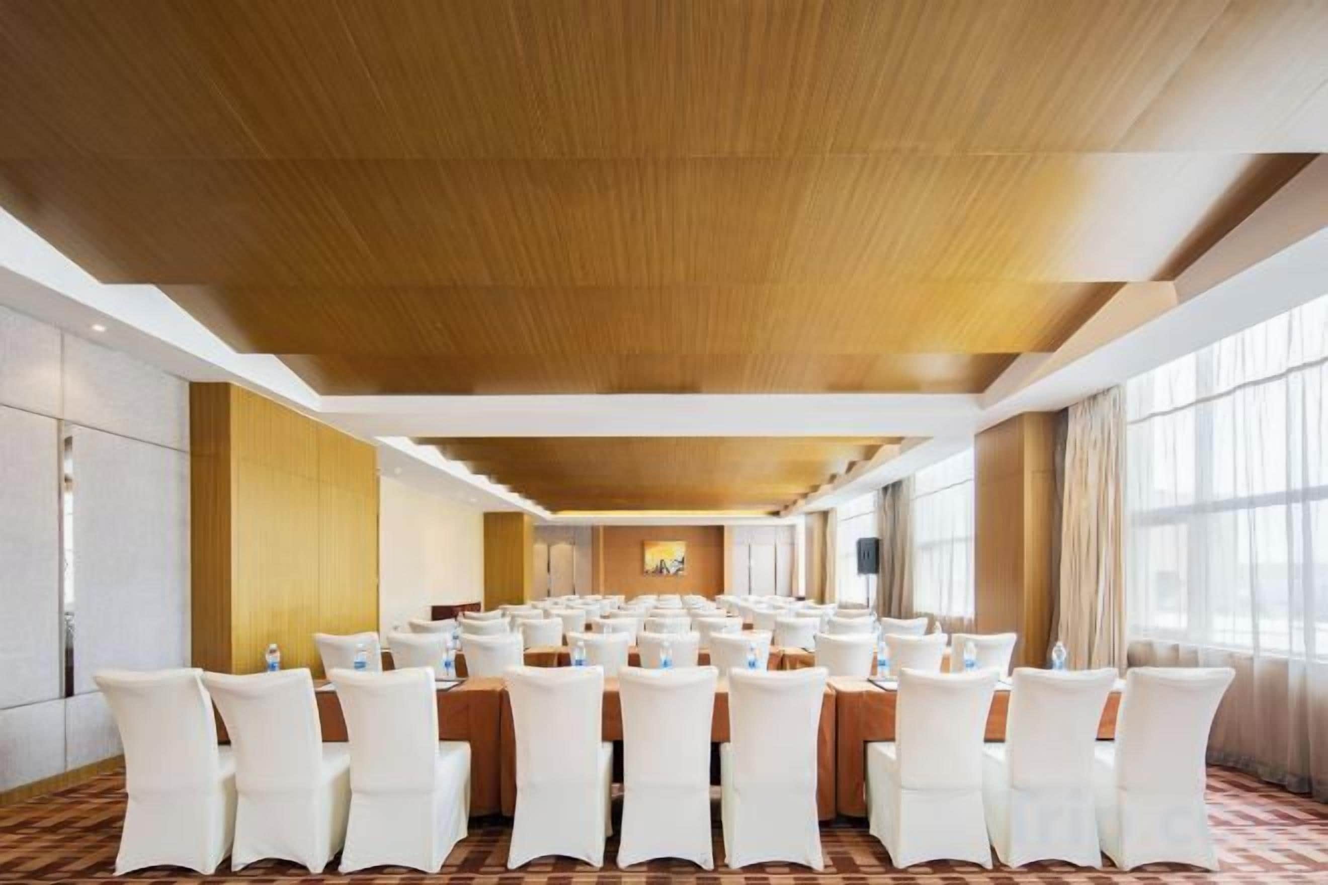 A conference room with multiple tables and chairs, large windows, and a wooden ceiling.