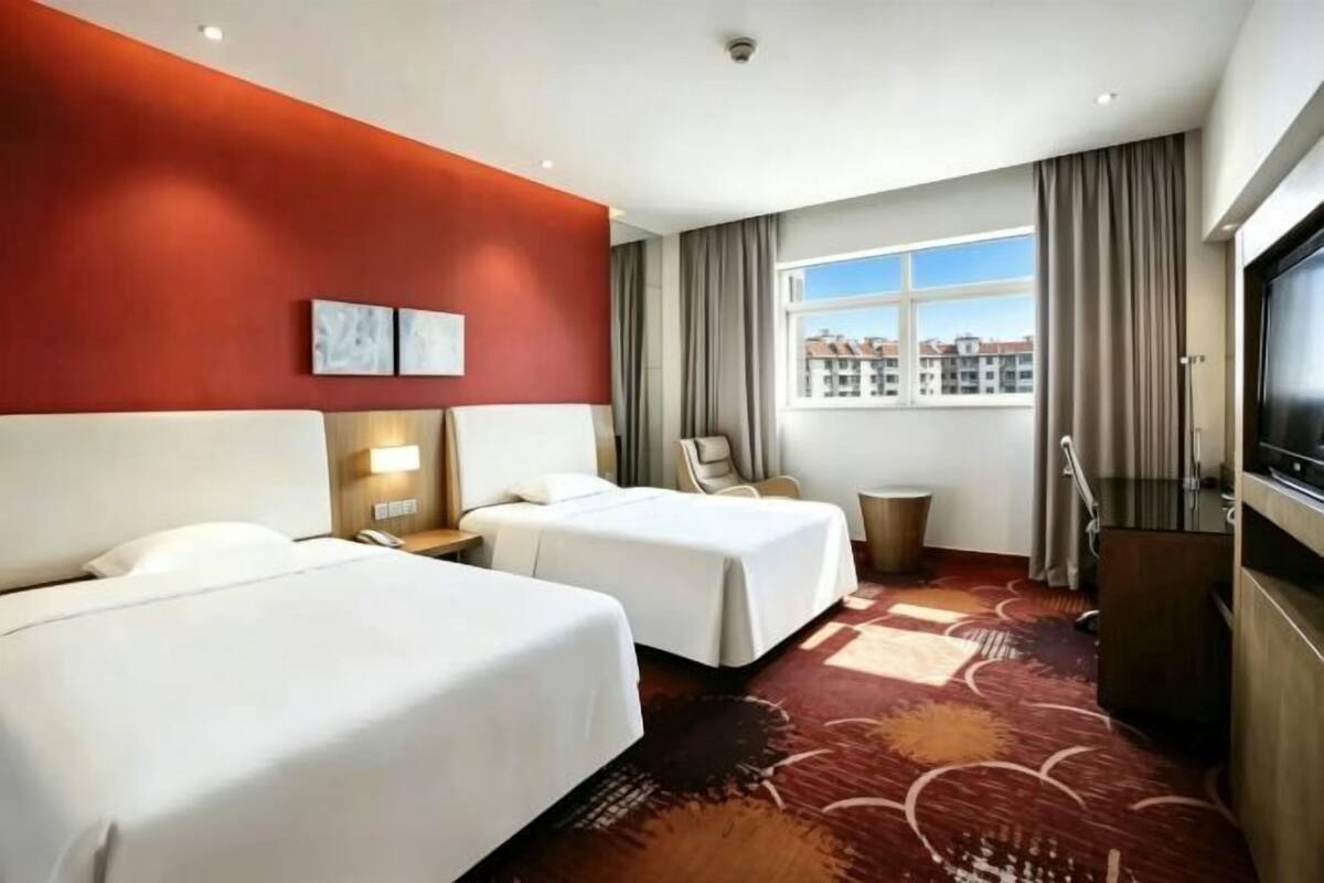 Een hotelkamer met twee bedden, een televisie, een bureau en een raam met uitzicht over de stad.