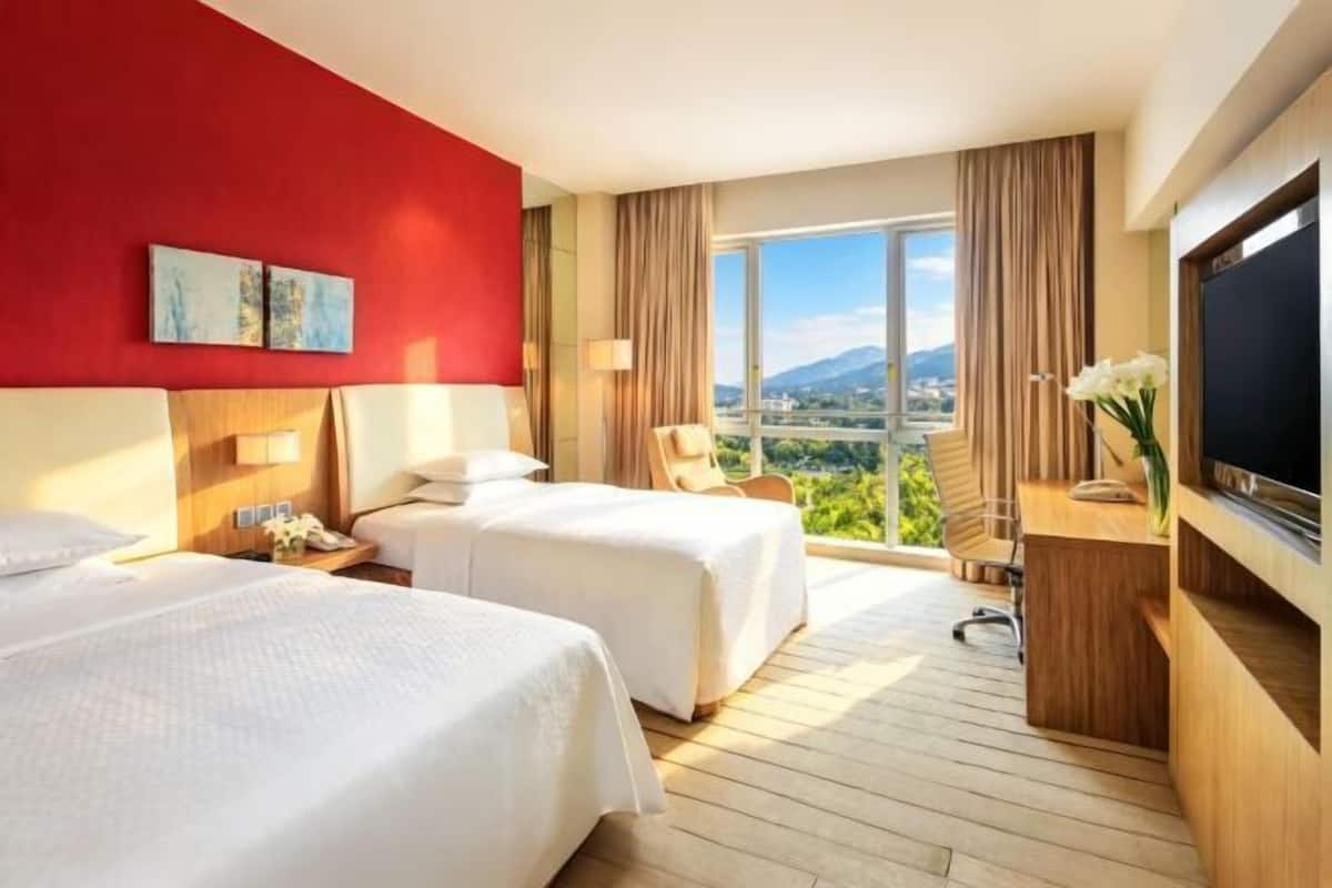 Een hotelkamer met twee bedden, een televisie, een bureau en uitzicht op een stadsgezicht.