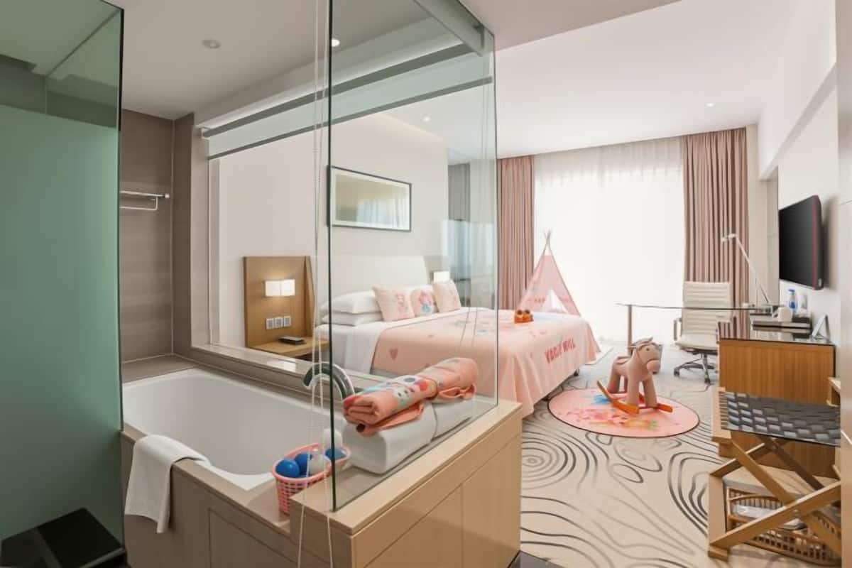 Een moderne hotelkamer met een douchecabine van glas, een bed met een roze hemelbed, een bureau met een stoel en een televisie.