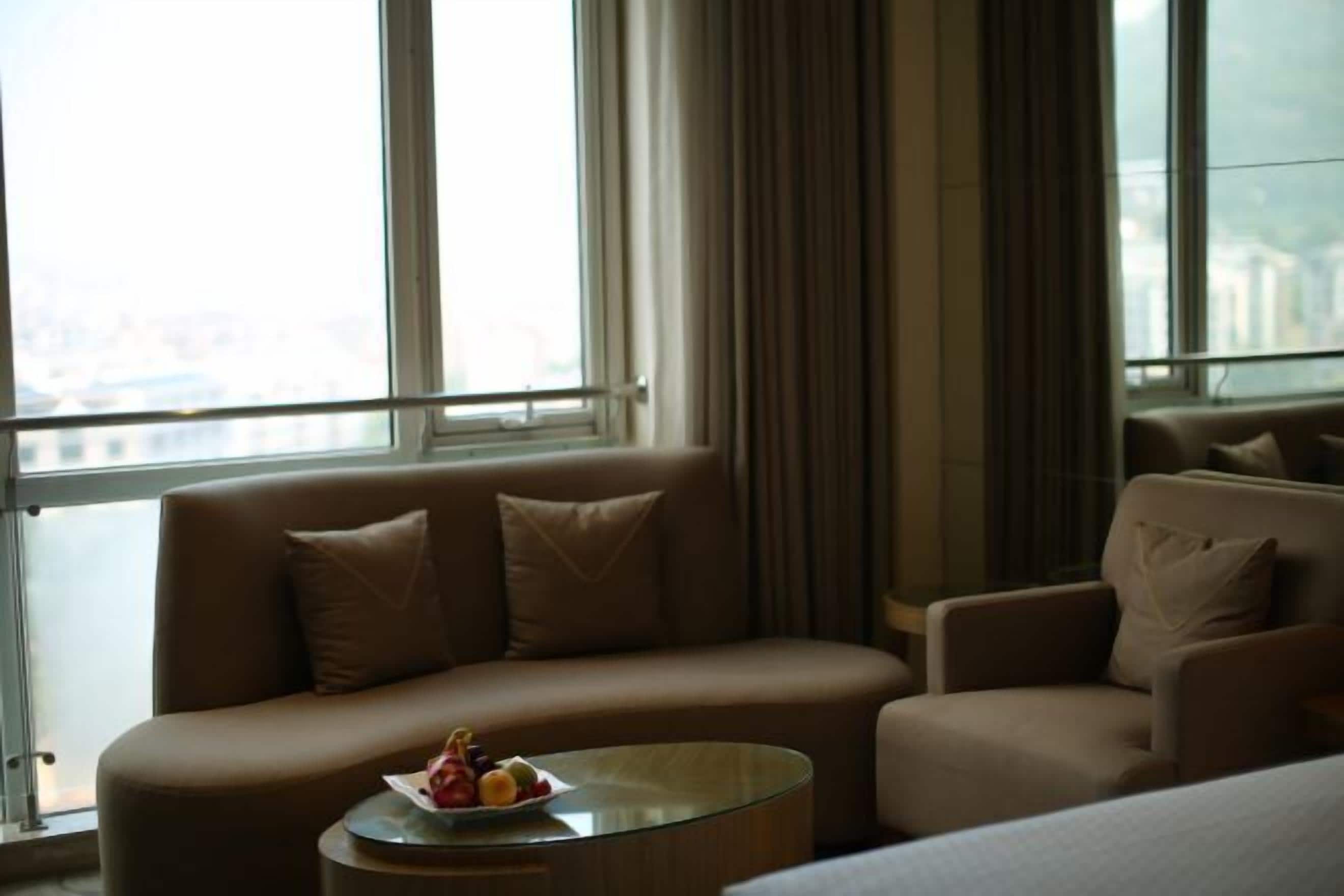 A modern hotel room with a sofa, armchair, and a small round table with fruit.