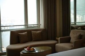 Una camera d'albergo moderna con divano, poltrona e un piccolo tavolino con frutta.