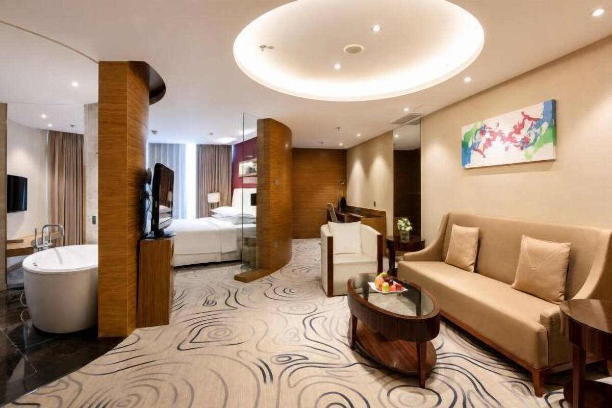 Een moderne hotelkamer met een groot bed, een zithoek met een bank en een salontafel, een ligbad en een groot raam.