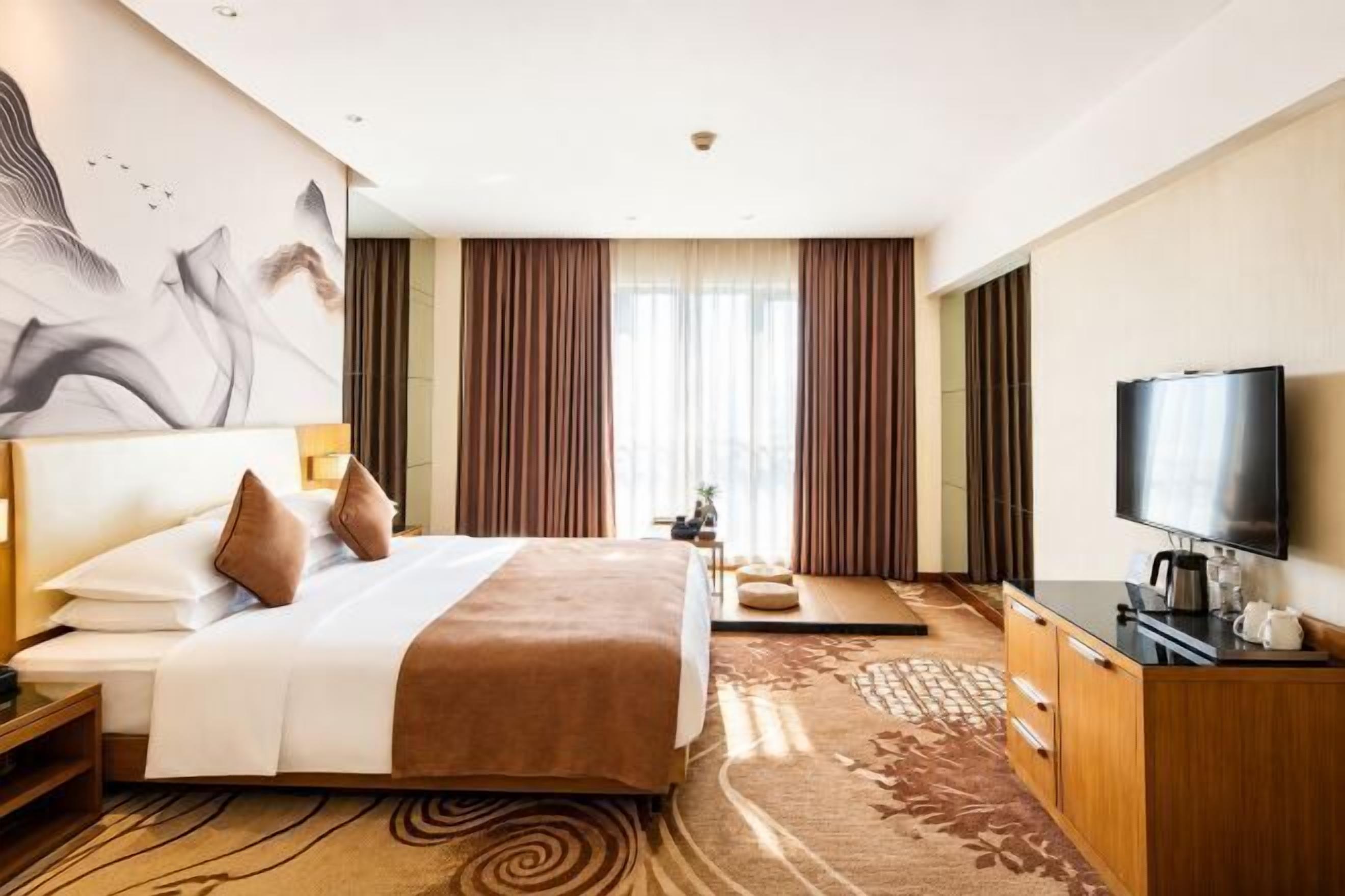 A hotel room with a large bed, a television, a desk, and a view of the outdoors.