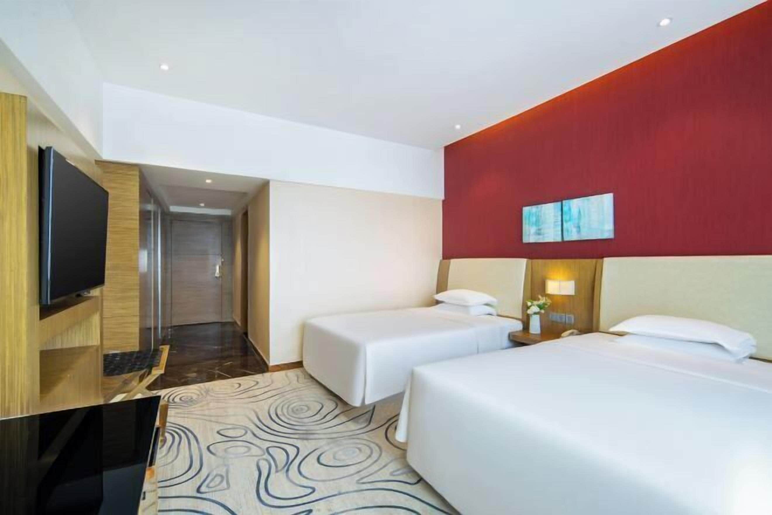A hotel room with a TV, two beds, a shower area, and a red accent wall.