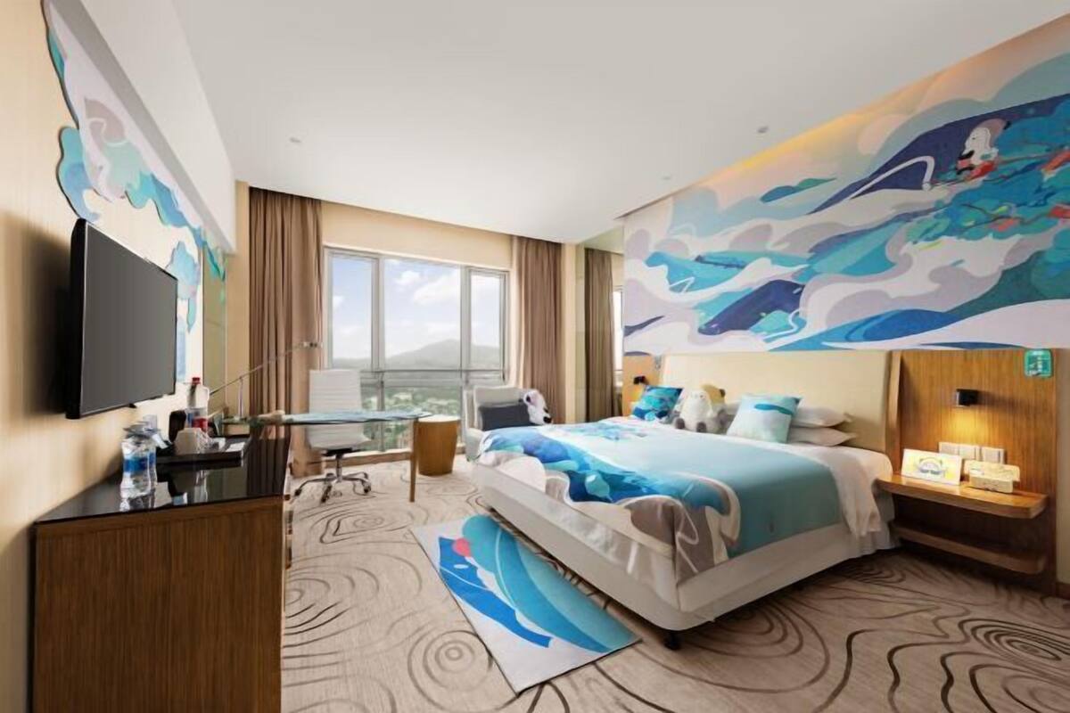 Een hotelkamer met een bed, een bureau, een televisie en een groot raam.