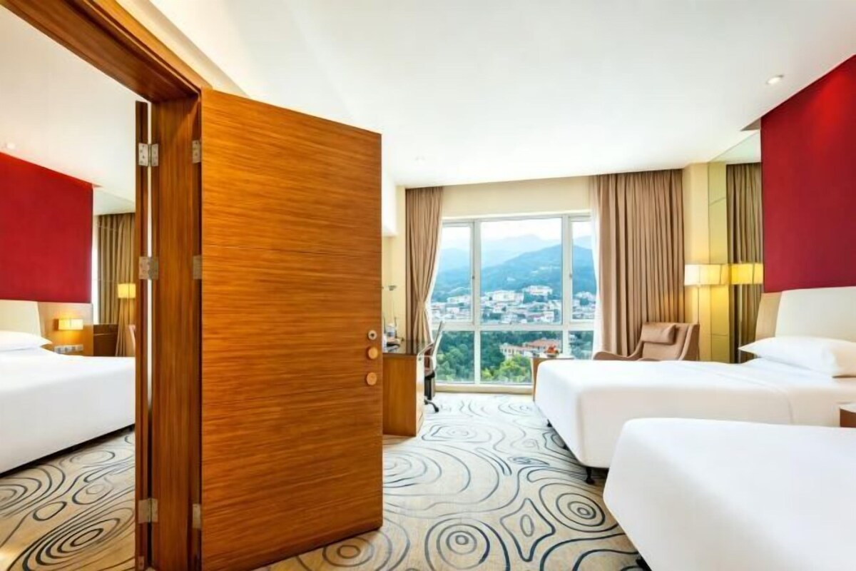 Une chambre d’hôtel avec deux lits, une grande fenêtre donnant sur la ville et une porte en bois.