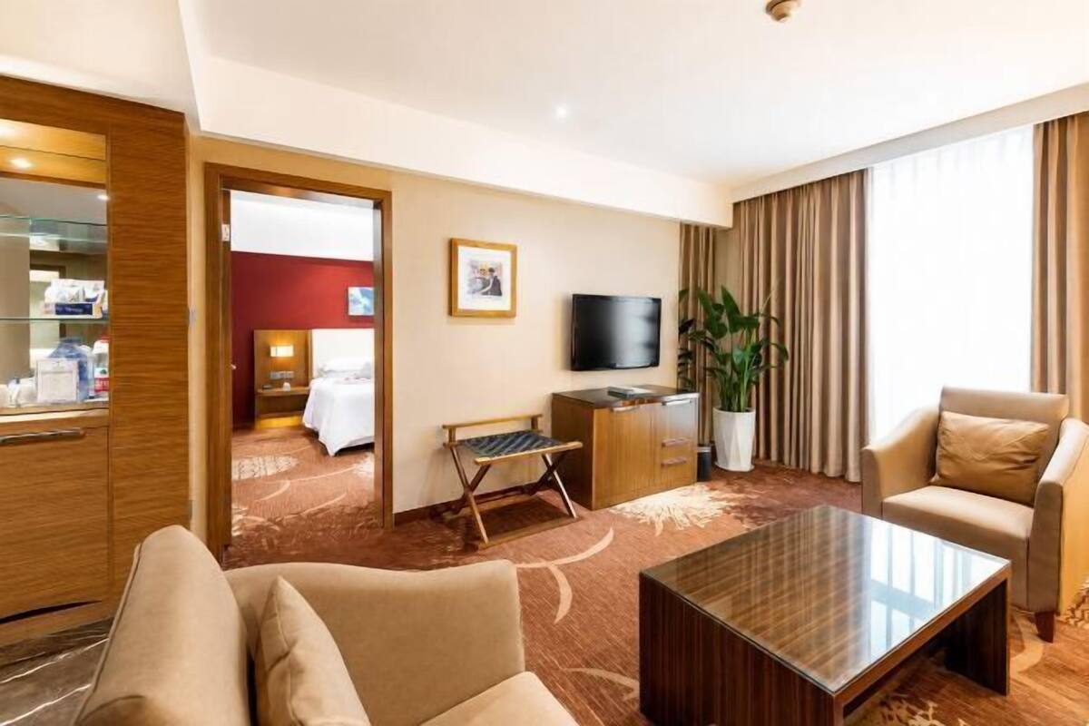 Habitación de hotel con sala de estar, televisión, sofá, mesa de centro, escritorio y cama.