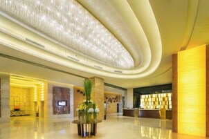 A modern hotel lobby with a curved ceiling, a reception desk, and a seating area with a vase of flowers.