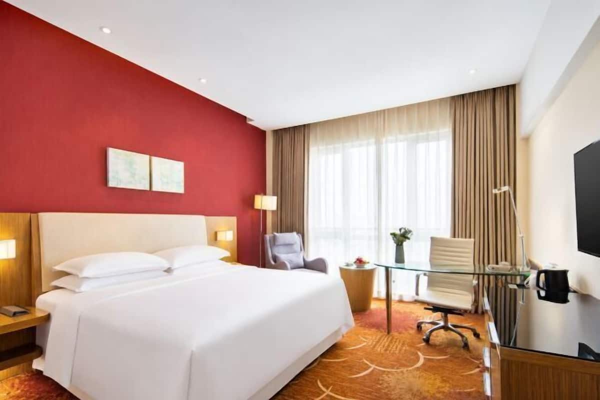 Een hotelkamer met een groot bed, een bureau met stoel, een televisie en een raam met gordijnen.