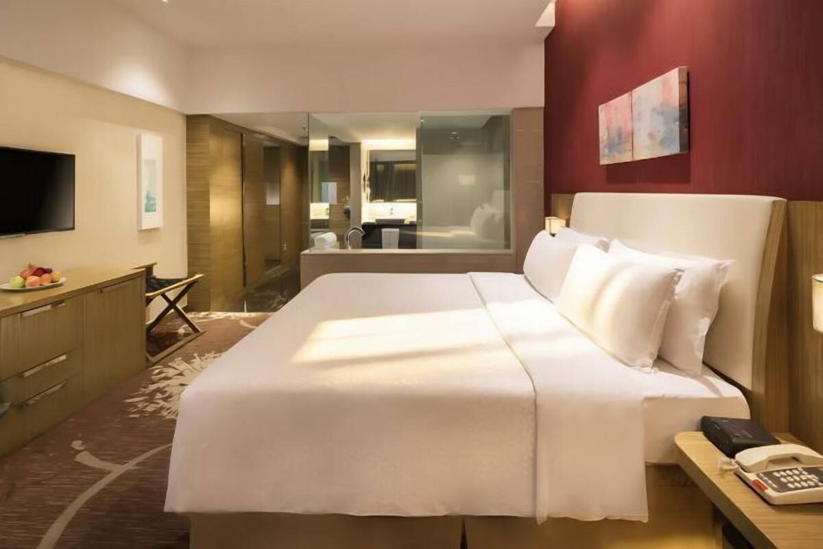 Hotelkamer met een bed, een bureau met telefoon, een televisie en uitzicht op een badkamer en gang.