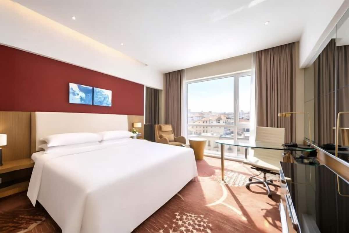 Een hotelkamer met een groot bed, een bureau met stoel, uitzicht over de stad en een balkon.