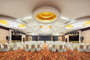 Une grande salle de conférence avec des tables et des chaises rondes, une moquette à motifs et un lustre moderne.