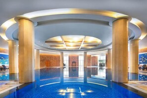Une vaste piscine intérieure de forme circulaire, entourée de colonnes et surmontée d’un haut plafond.