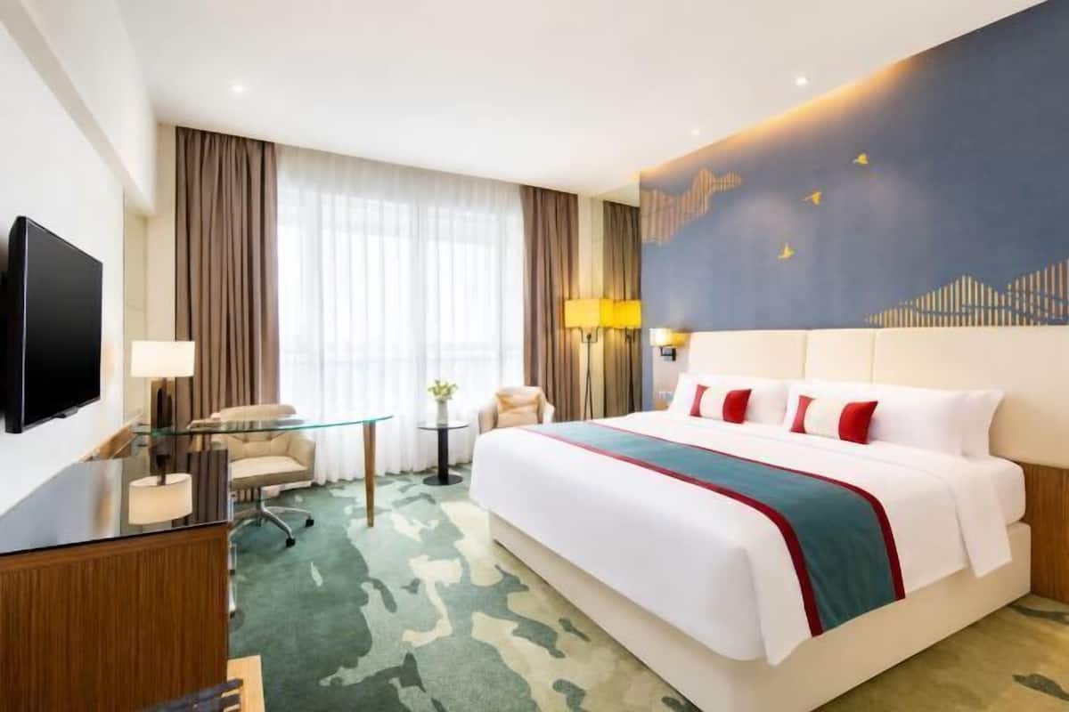 Een hotelkamer met een groot bed, een bureau met stoel, een televisie en een raam met gordijnen.