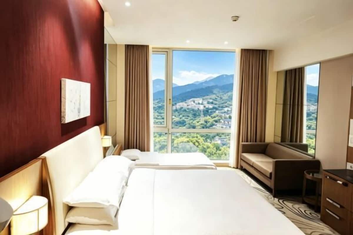 Hotelkamer met een groot bed, een bureau, een stoel en uitzicht op een stad en bergen.