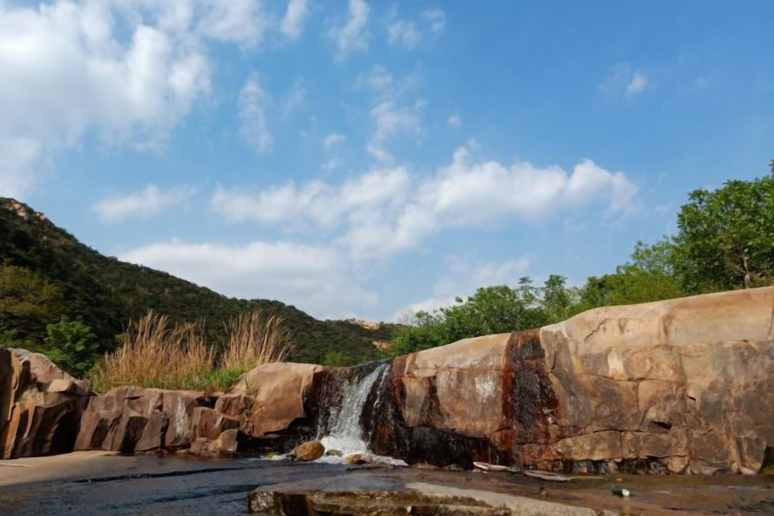 A natural landscape with a waterfall, rocky terrain, and a clear sky.