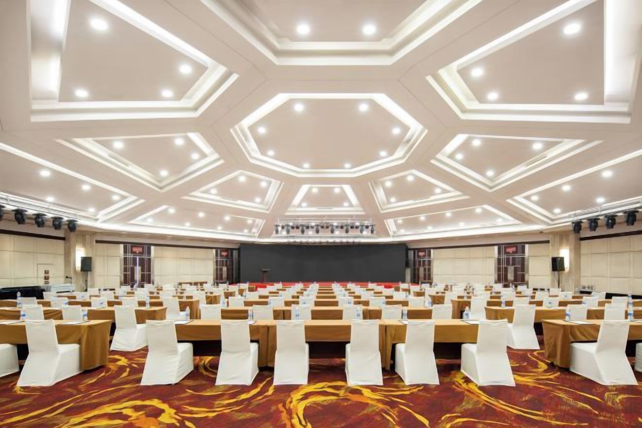 A conference room with rows of tables and chairs, a stage, and a large screen.