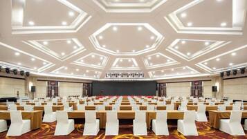 A conference room with rows of tables and chairs, a stage, and a large screen.