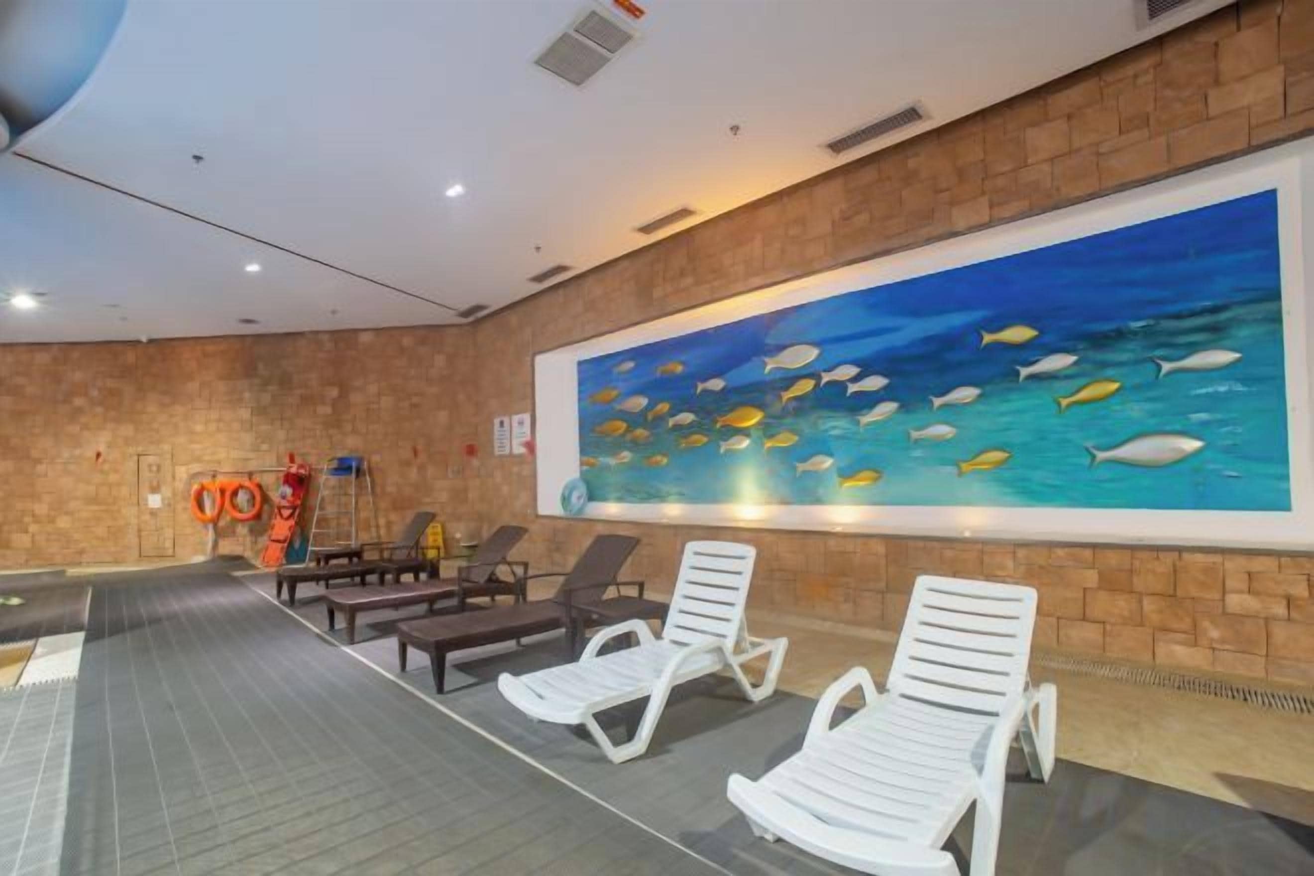 Zona de piscina con sillones de descanso, un puesto de socorrista y un mural de peces en la pared.