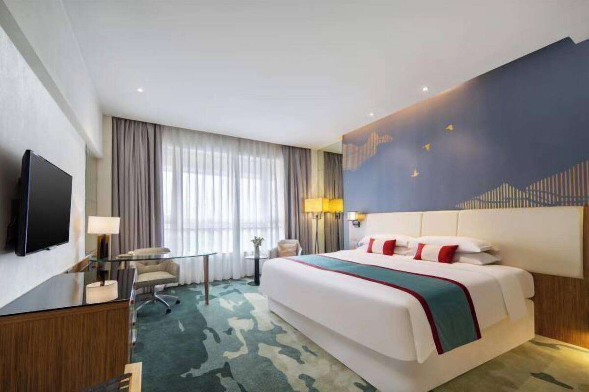 Een hotelkamer met een groot bed, een flatscreen televisie, een bureau met lamp en uitzicht op de stadshemel door het raam.