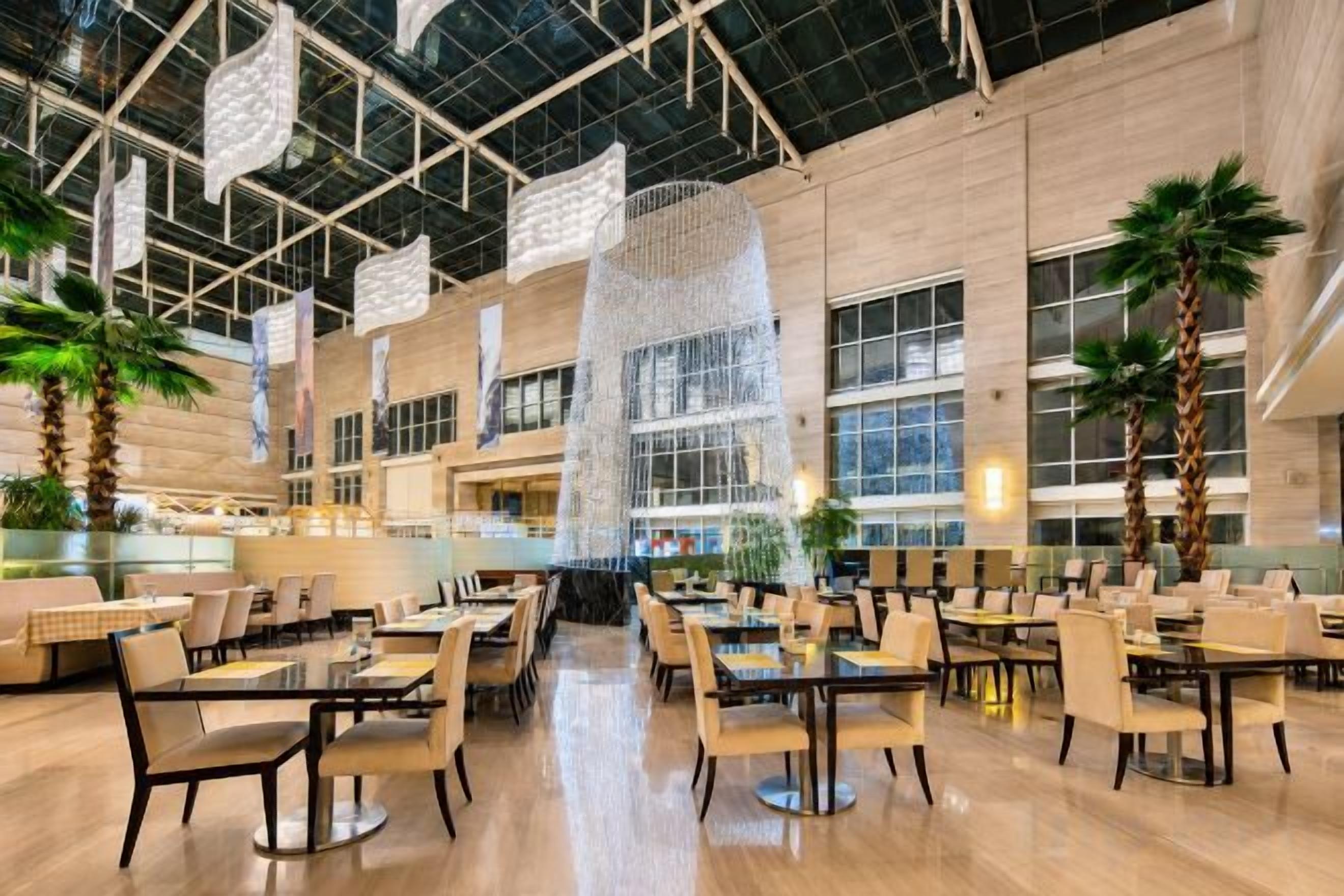 A spacious indoor dining area with multiple tables and chairs, large windows, and a high ceiling with hanging decorations.