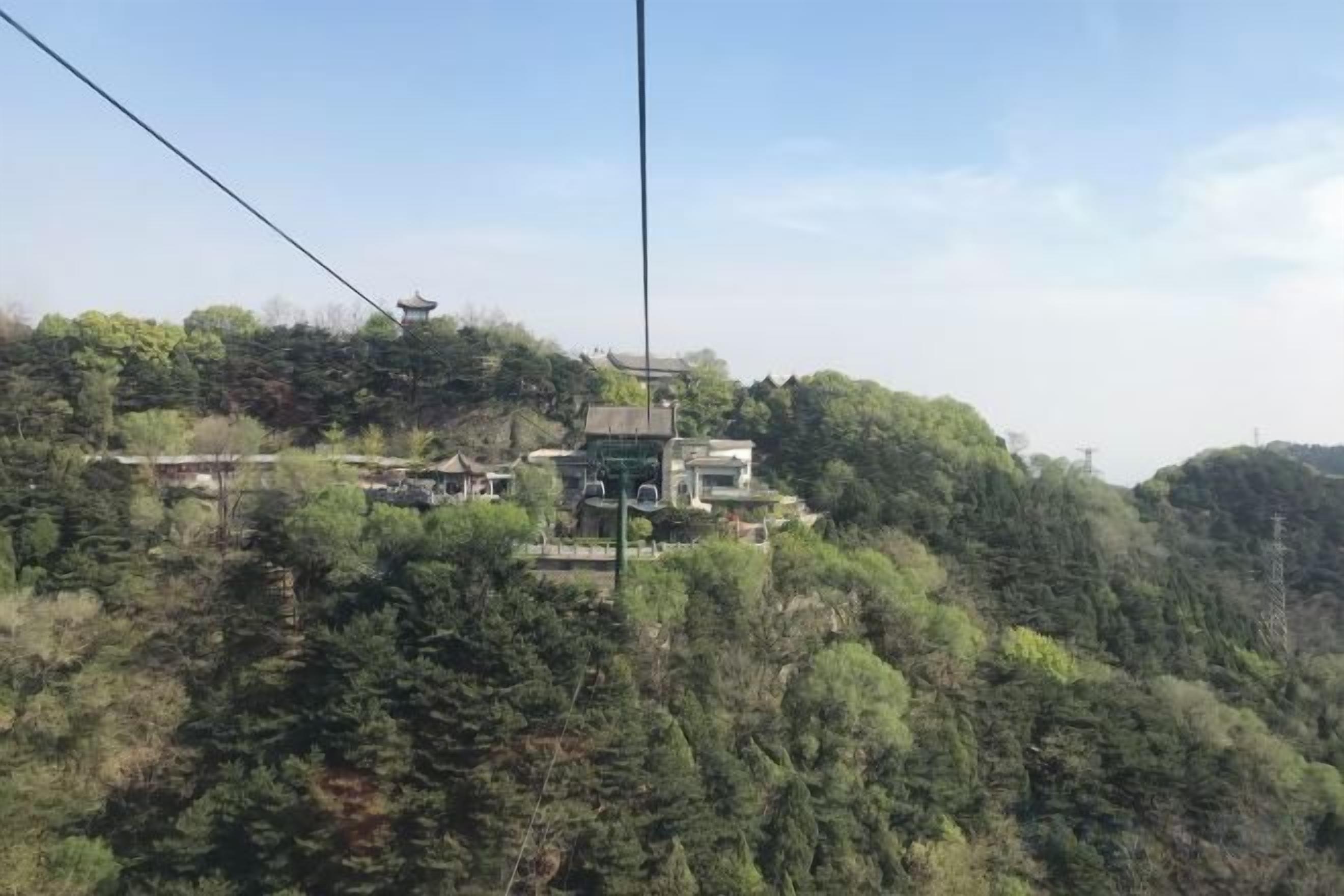 Sistema de teleférico con un edificio tradicional en la cima de una colina, rodeado de bosque denso.