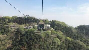 Sistema de teleférico con un edificio tradicional en la cima de una colina, rodeado de bosque denso.