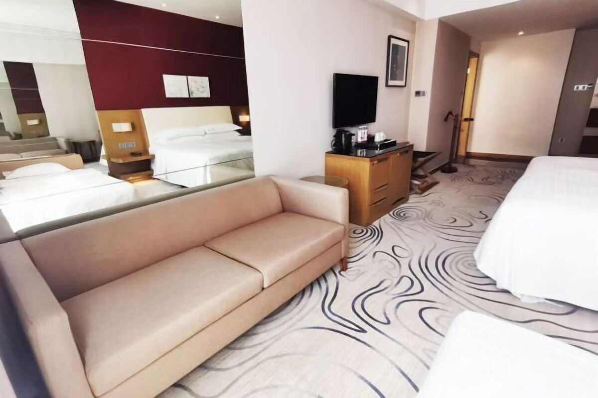 Una camera d'albergo con un letto, un divano, una TV, un comò e uno specchio.