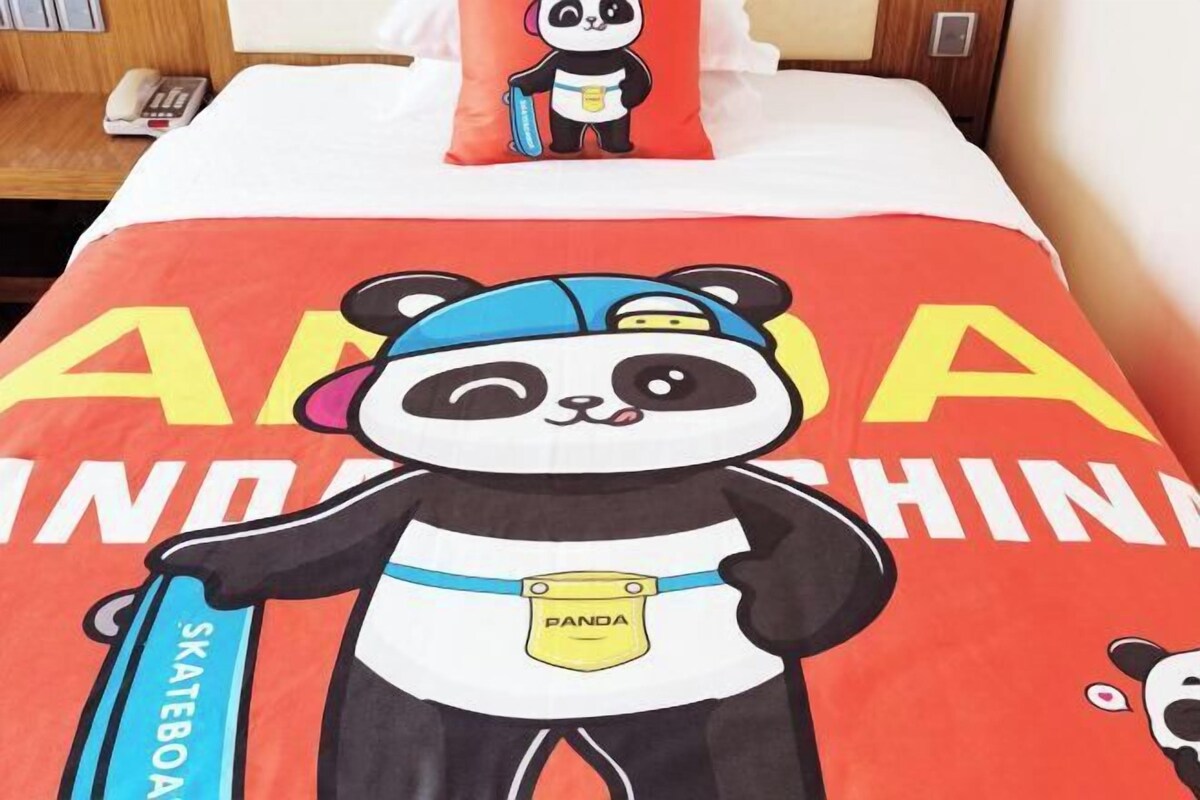 Un letto con copripiumone a tema panda, un cuscino con un disegno di panda e un comodino con un telefono.