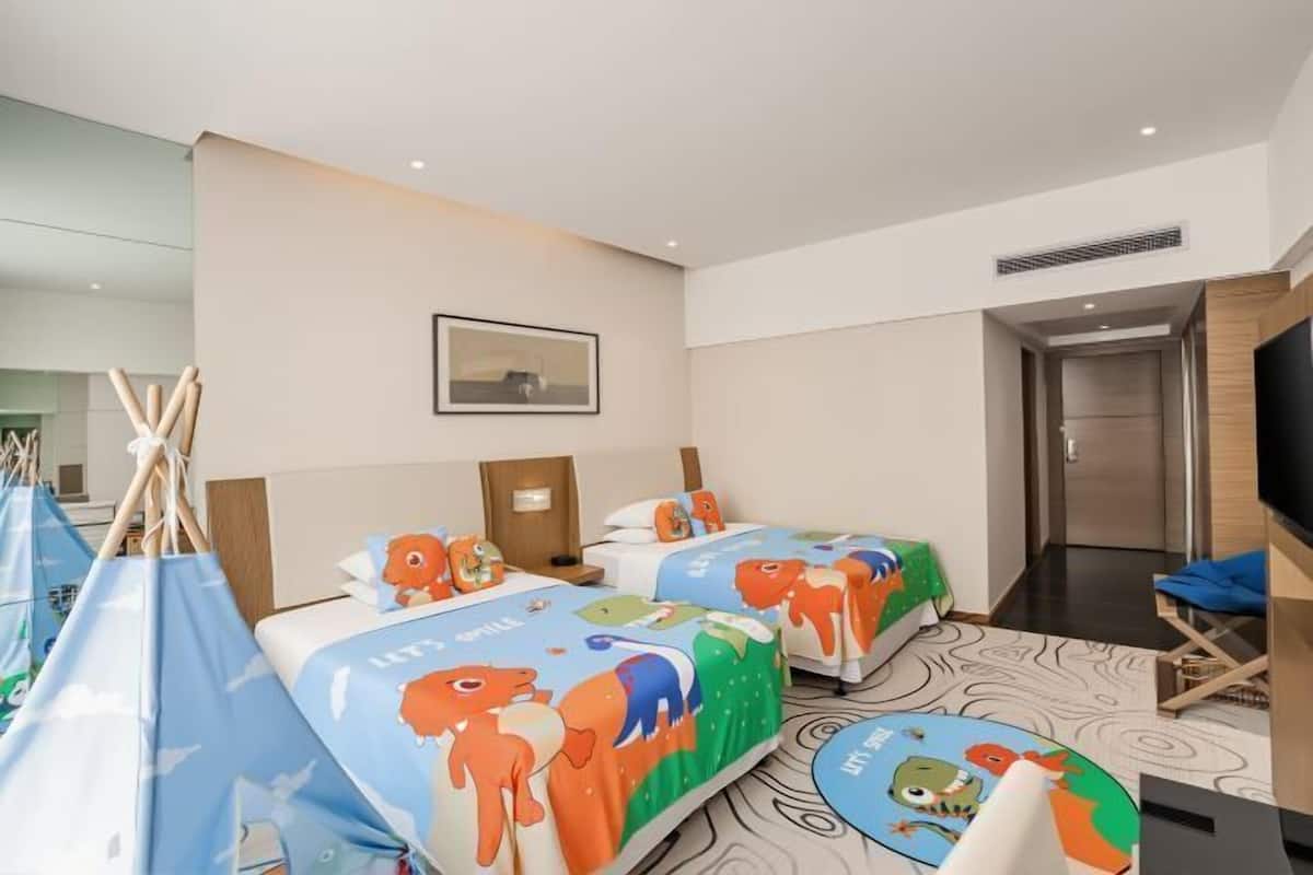 Een hotelkamer met twee bedden, een televisie, een spiegel en een deur naar een gang.