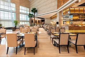 Un comedor amplio con varias mesas y sillas, una zona de bar con mostrador, y ventanas grandes que permiten la entrada de luz natural.