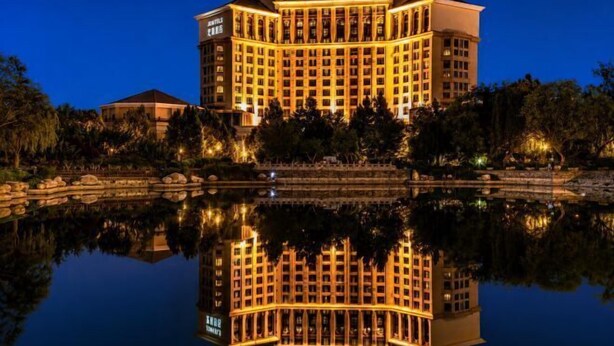 Un grand hôtel illuminé, dont le reflet se mire dans l’eau, entouré d’arbres et bordé d’un petit étang.