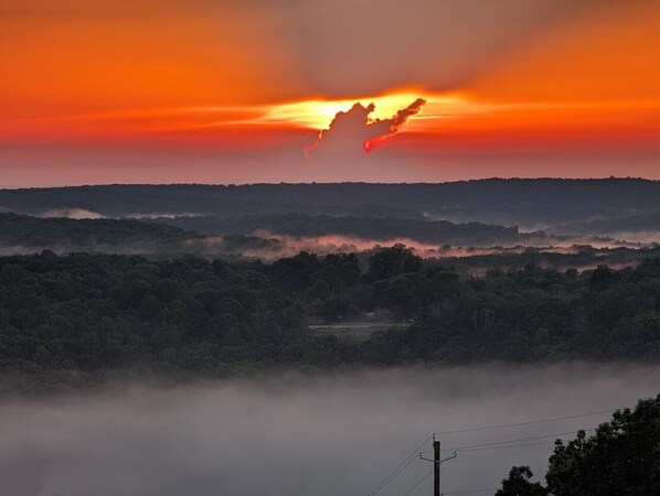 Een zonsopgang boven een bebost landschap, met een weg en elektriciteitskabels.