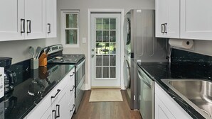 Una cocina con gabinetes blancos, encimera negra, refrigerador de acero inoxidable y puerta que da a un patio.