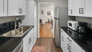 Una cocina moderna con armarios blancos, un lavamanos de acero inoxidable, una encimera negra y un refrigerador.