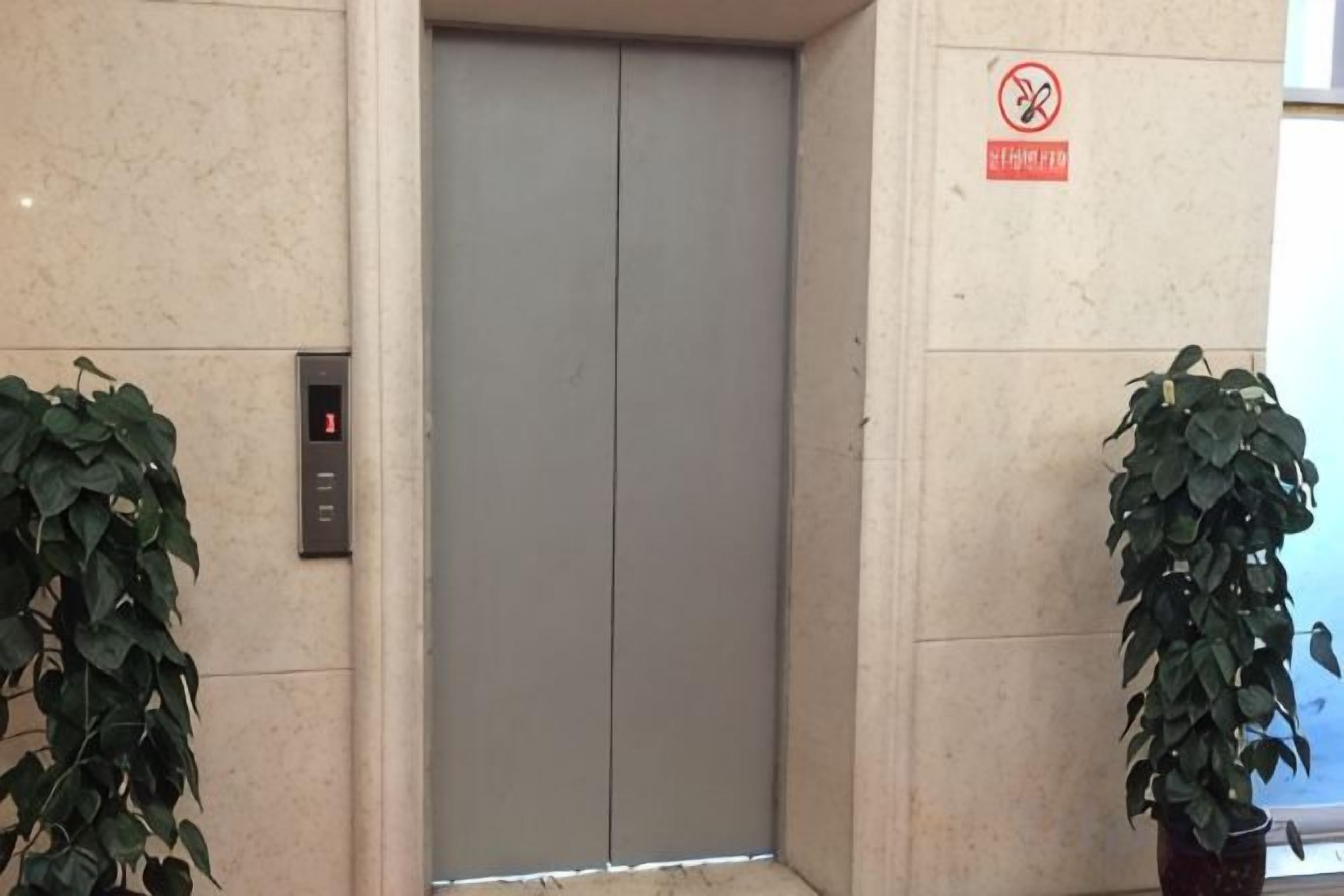 An elevator with a digital display, a no smoking sign, and potted plants.