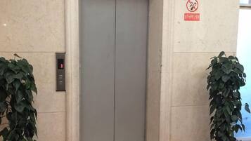 An elevator with a digital display, a no smoking sign, and potted plants.