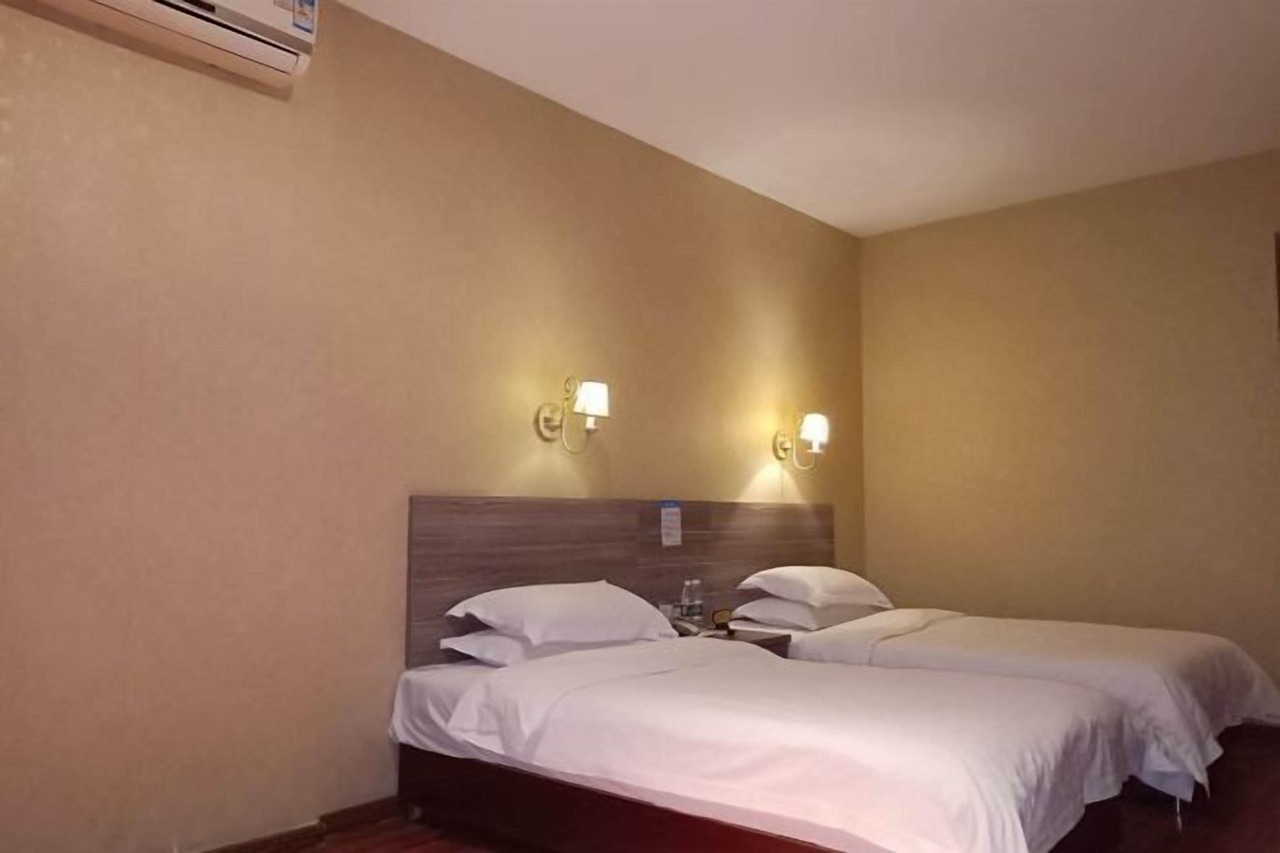 Camera d'albergo con due letti singoli, un poggiatesta in legno, lampade a parete e un condizionatore d'aria.