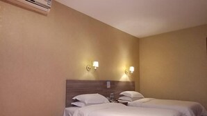 Una habitación de hotel con dos camas individuales, un cabecero de madera, lámparas fijadas a la pared y un equipo de aire acondicionado.