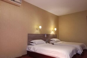 Una habitación de hotel con dos camas individuales, un cabecero de madera, lámparas fijadas a la pared y un equipo de aire acondicionado.