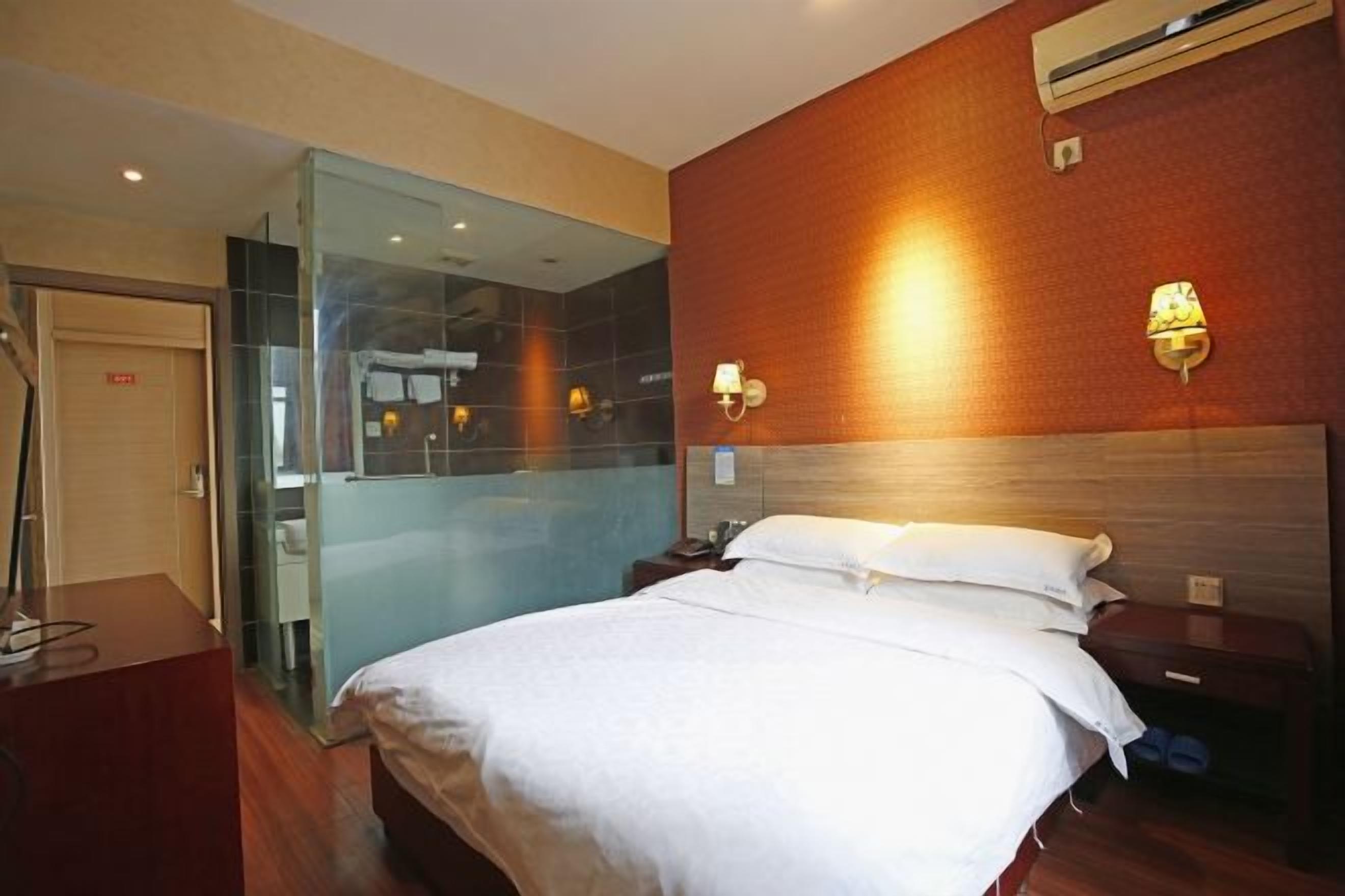 A hotel room with a bed, bedside tables, a mirror, and an air conditioning unit.