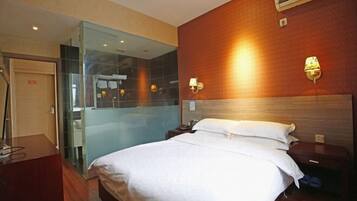 A hotel room with a bed, bedside tables, a mirror, and an air conditioning unit.