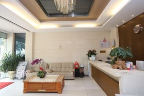 A hotel lobby with a reception desk, a sofa, a coffee table, and potted plants. - Blue City Exepress Hotel (Chengdu)