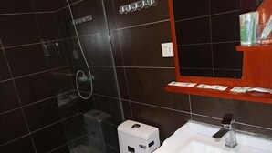 Un baño con cabina de ducha de vidrio, un lavabo blanco con grifo moderno y un estante con artículos de aseo.