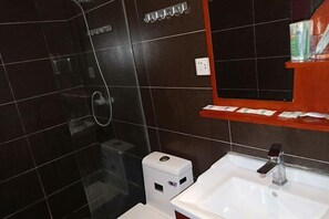 Un baño con cabina de ducha de vidrio, un lavabo blanco con grifo moderno y un estante con artículos de aseo.