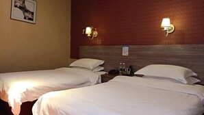 Habitación de hotel con dos camas, cabecero de madera, lámparas de pared e imagen enmarcada.